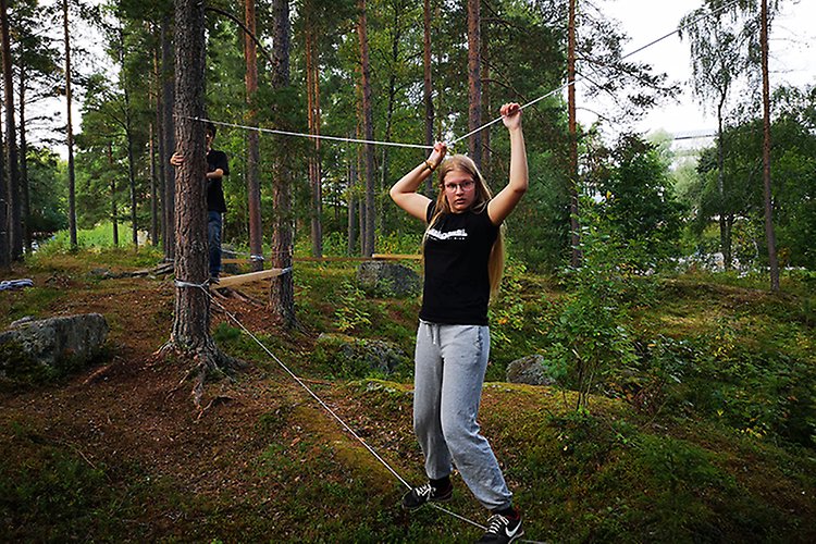 Hinderbana i skogen på idrottslektionen. En elev går balansgång på ett rep som är uppspänt mellan två träd. 