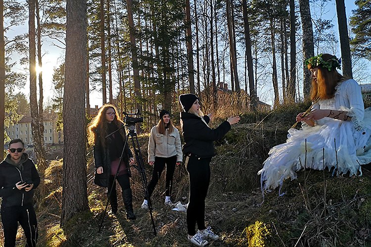 En kortfilm spelas in i skogen. En elev är klädd i en vit klänning och agerar framför kameran. På bilden syns ytterligare fyra elever som jobbar bakom kameran med att filma och ge regi. 
