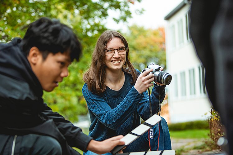 Två elever på estetiska programmet är utomhus och jobbar med film. En elev håller i en kamera. Den andra eleven håller i en filmklappa. 